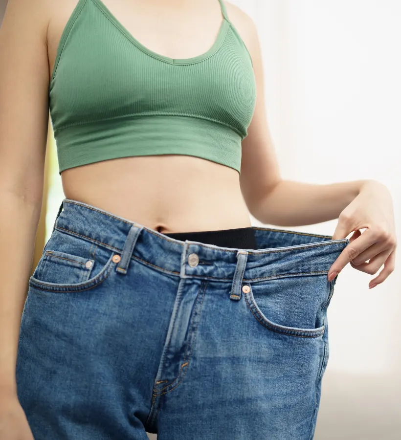 A patient celebrating weight loss progress with loose-fitting jeans
