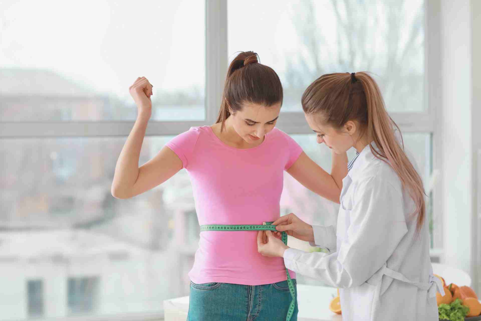 Medical Professional Measuring Waist of Young Woman in Weight Loss Clinic
